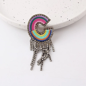 Detailed shot of G-letter brooch with rainbow embroidery and hanging crystal tassels