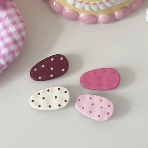 Close-up of four colorful polka dot hair clips with glossy ceramic finish on fabric