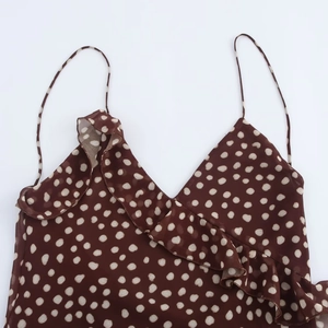Brown polka dot summer dress with spaghetti straps and ruffle detail on a white background