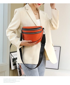 Detail of an orange crossbody bag with dual black zippers and adjustable wide strap