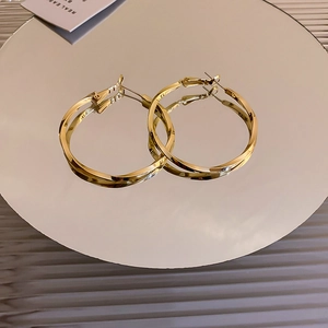 Detailed view of gold twisted metal hoop earrings on mirror reflecting elegant texture