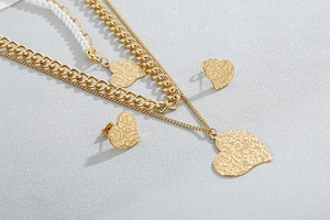 Detail of layered gold necklace with pearl chains and textured heart pendants and earrings
