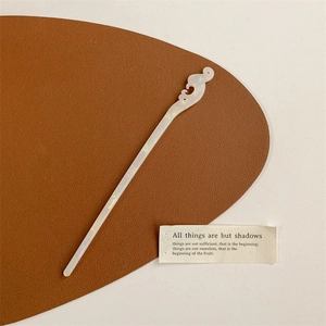 Detailed shot of a white pearlescent cloud-shaped hair pin on a brown leather mat