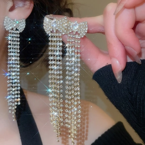 Detailed view of silver bow earrings with long sparkling tassel drapes held by hand