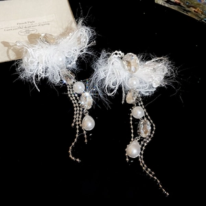 Detail of long tassel earrings with white feathers, pearls, and crystals on a black background