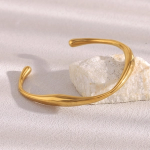 Detailed close-up of an irregular twisted 18K gold plated bangle on a white stone pedestal