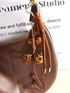 Detail of a brown leather bag with leopard print bow and heart beaded charm pendant