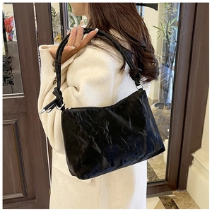 Detail of glossy black shoulder bag featuring unique pleated leather texture and knot strap