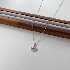 Detailed close-up of a silver Evil Eye pendant with blue stone on wooden display