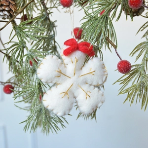 White felt snowflake Christmas ornament with gold embroidery and red bow on pine branch