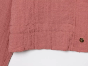 Detail of rose pink jacket with linen texture and golden metal snap fastener