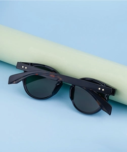 Detail of oval black frame sunglasses with metal star rivets on light green stand