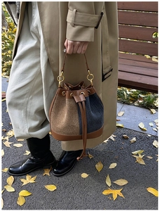 Detail view of denim and suede bucket bag with drawstring closure and gold metal rings