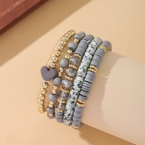 Detail of bohemian layered bracelets with grey clay discs and golden heart charm