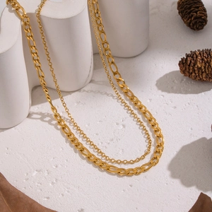 Detail of gold double-layered Figaro chain necklace on a minimalist aesthetic background