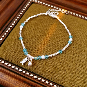 Detail of silver beaded bracelet with pearls and fish pendant on a vintage wood tray