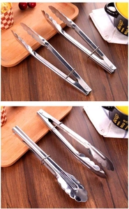 Detail of stainless steel food tongs with wavy heads and locking mechanism on wood
