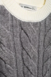 Close-up of knit sweater vest neckline showing white trim and cable stitch texture