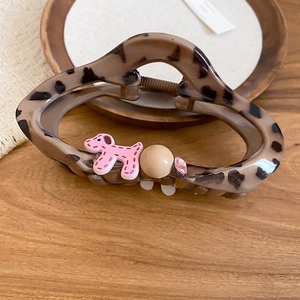 Detail of leopard print hair claw with pink puppy and pearl on a wooden surface