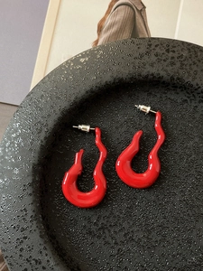 Detail of red flame-shaped wavy earrings with glossy finish on a textured stone tray