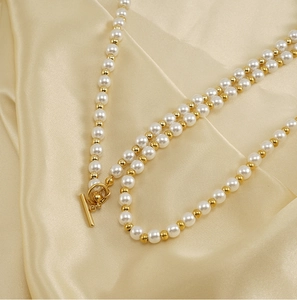 Détail d'un collier de perles blanches et billes dorées avec fermoir à bascule OT