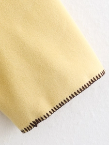 Macro shot of pale yellow wool fabric with brown blanket stitch detailing on the edge