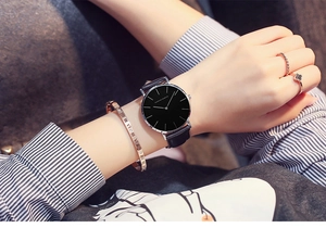 Close-up of elegant black leather watch paired with gold Roman numeral bangle and rings