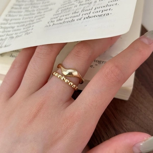 Close-up of gold irregular wavy ring and beaded band set worn on hand on warm background