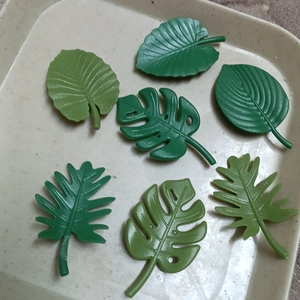 Set of 7 artificial green monstera and fern leaf fridge magnets on a beige tray
