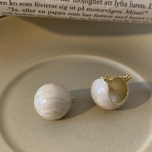 Detail of cream enamel and gold asymmetric earrings with irregular ripple texture on ceramic