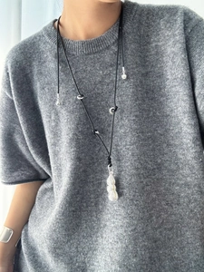 Long necklace with silver peanut-shaped pendant on black cord worn on grey sweater