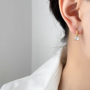 Close-up of golden hoop earrings with a sparkling round zircon in a four-prong setting