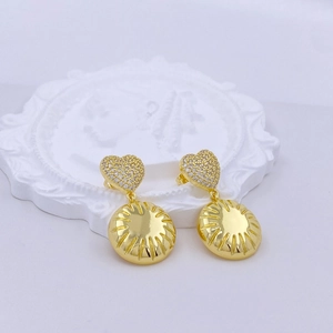 Macro detail of gold heart earrings with white zircon pavé and sunburst texture pendant