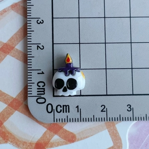 Detailed size view of a miniature resin skull bead with a purple candle and flame