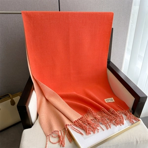 Detail showing the orange and pink cashmere-like scarf with fringe and design label