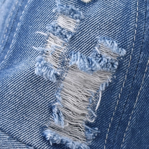 Macro view of blue distressed denim fabric with detailed frayed edges and twill texture