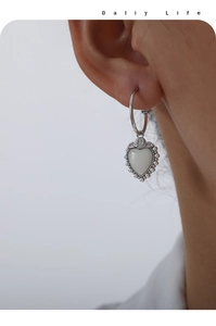 Detailed close-up of a heart-shaped pearl earring with elegant floral relief on model's ear