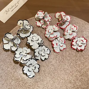 Floral stud earrings with hand-painted black and red edges on a soft brown display tray