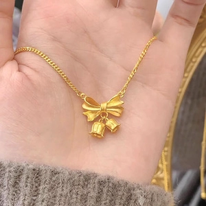 Detailed view of a gold bow and bell pendant necklace held in hand to show size