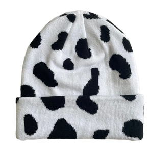 Detailed flat lay view of a black and white cow print knitted beanie with wool texture
