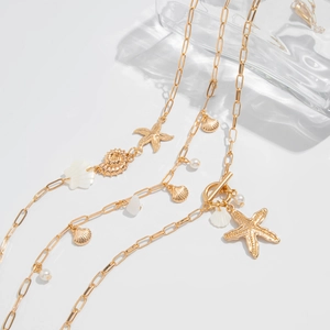 Detailed shot of gold starfish and shell pendants with pearls on layered flat snake chains