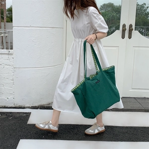 Deep green canvas tote bag with green checkered lining shown in casual outdoor street setting