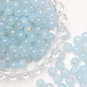 Macro shot of 8mm light blue glass beads with gold texture in a decorative glass bowl