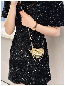 Golden metal lip-shaped mini crossbody bag with bead chain shown on black sequin dress