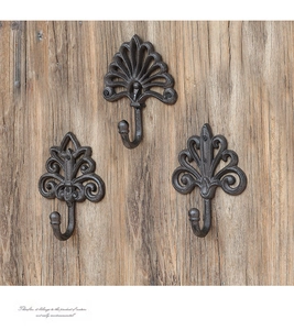 Detailed view of three vintage black cast iron wall hooks with floral patterns on wood