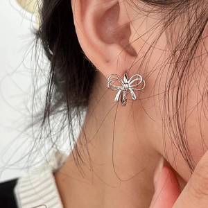 Close-up of a silver bow-shaped earring worn on ear showing polished metallic finish