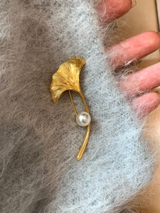 Macro di una spilla a foglia di ginkgo placcata oro 18K con venature e perla bianca