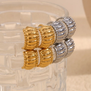 Detail of twisted gold and silver hoop earrings on a textured glass rim