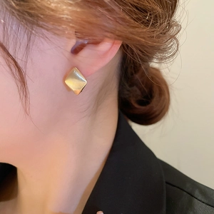 Détail d'une boucle d'oreille losange plaquée or avec une surface en métal brossé