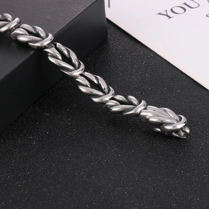 Close-up of a silver stainless steel knot link chain bracelet on a black textured surface